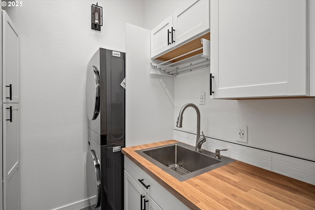 kitchen featuring butcher block counters, a sink, white cabinets, and stacked washer / drying machine