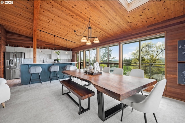 dining room with a skylight, light carpet, wood walls, high vaulted ceiling, and wooden ceiling