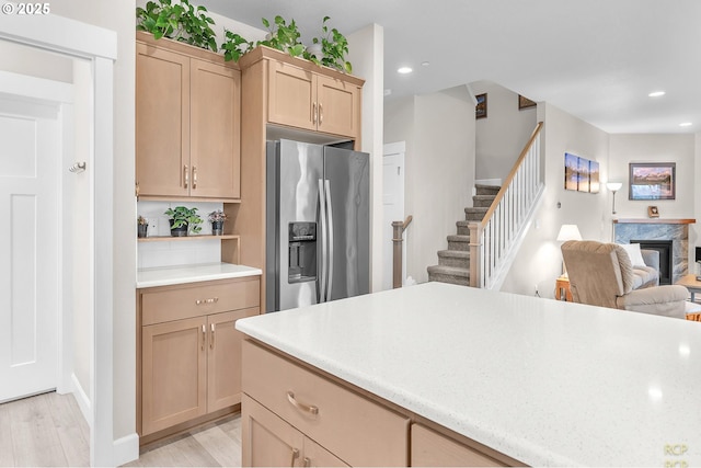 kitchen featuring light brown cabinets, stainless steel fridge with ice dispenser, open floor plan, light wood-style flooring, and a fireplace