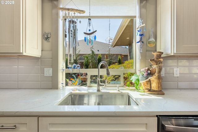 kitchen with backsplash, light stone countertops, a sink, and dishwasher