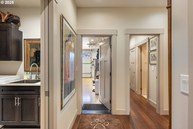hallway featuring dark wood finished floors, baseboards, and a sink