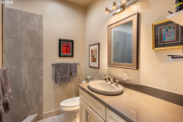 bathroom with toilet, wood finished floors, vanity, baseboards, and a tile shower