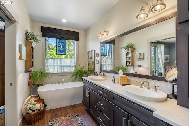 full bath with double vanity, a freestanding bath, a sink, and wood finished floors