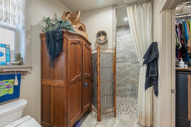 bathroom featuring toilet, a tile shower, and a closet