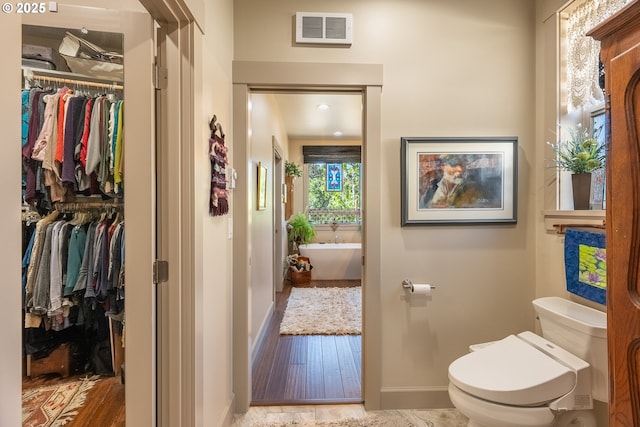 full bath featuring toilet, a freestanding bath, baseboards, and visible vents