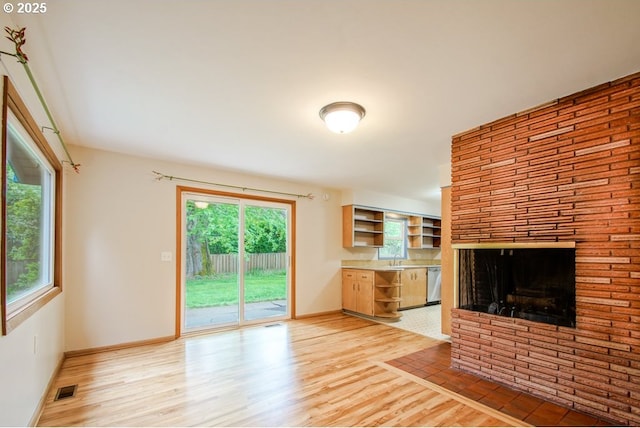 unfurnished living room with light wood-style flooring, baseboards, a fireplace, and a sink