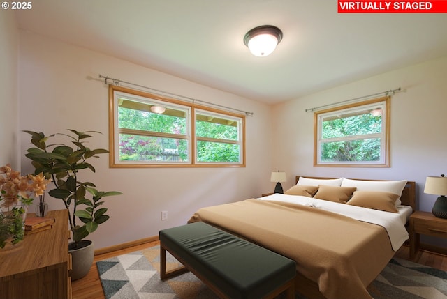 bedroom with multiple windows, wood finished floors, and baseboards