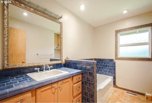 bathroom with a garden tub, baseboards, vanity, and recessed lighting