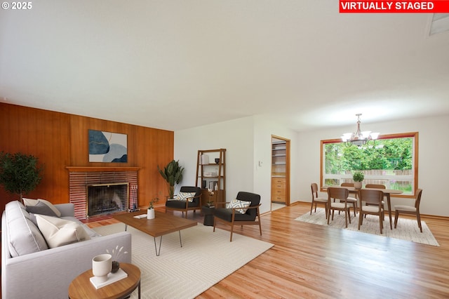living room featuring light wood finished floors, a brick fireplace, a chandelier, wooden walls, and baseboards