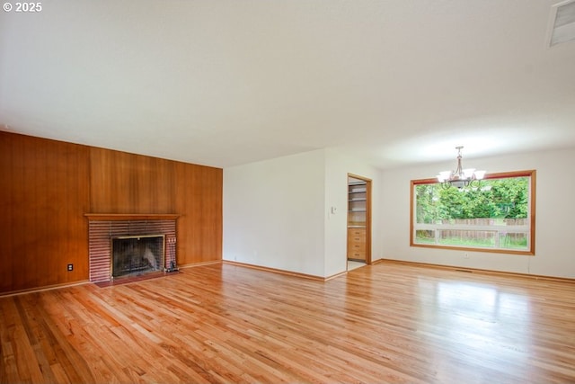 unfurnished living room with a chandelier, light wood-style floors, a brick fireplace, wood walls, and baseboards