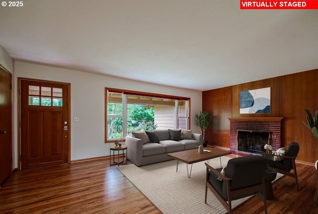 living room featuring wooden walls, wood finished floors, a fireplace, and baseboards