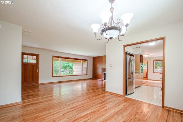 empty room with light wood-style flooring, a chandelier, plenty of natural light, and baseboards