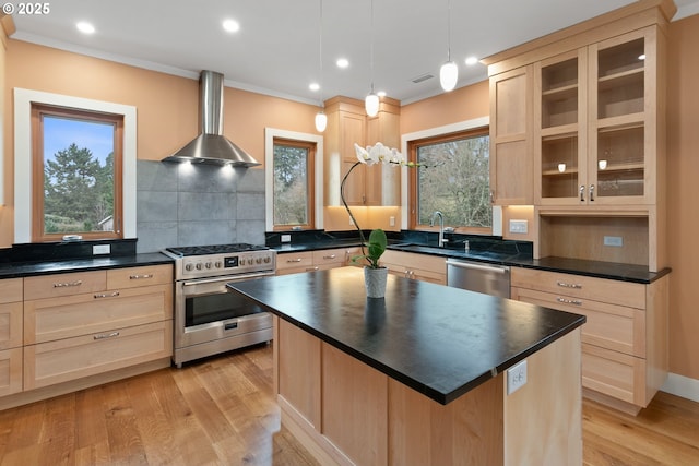 kitchen with stainless steel appliances, dark countertops, hanging light fixtures, a kitchen island, and wall chimney exhaust hood