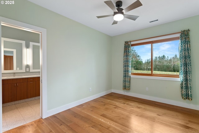 unfurnished room featuring ceiling fan, light wood-style flooring, a sink, visible vents, and baseboards