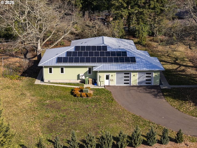 view of front of house featuring a garage, metal roof, solar panels, and a front yard