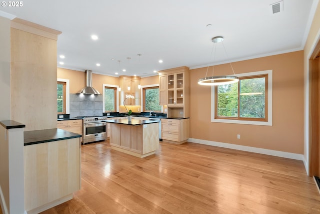 kitchen with stainless steel appliances, glass insert cabinets, hanging light fixtures, and wall chimney range hood