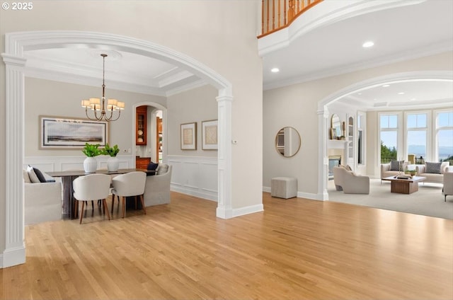 dining space featuring a chandelier, light wood-style floors, crown molding, a wainscoted wall, and a decorative wall