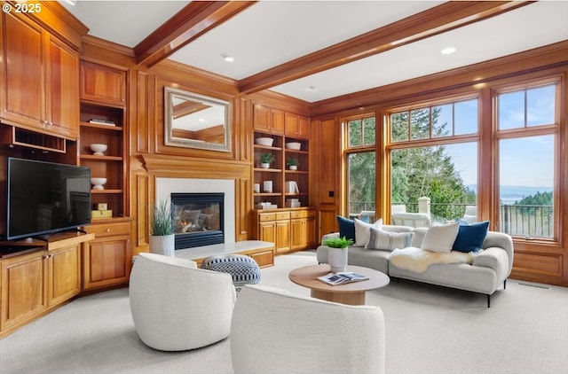 sitting room with light carpet, wooden walls, a glass covered fireplace, built in shelves, and crown molding