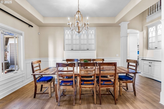 dining space with ornate columns, a tray ceiling, wood finished floors, and a wainscoted wall