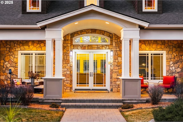 property entrance featuring stucco siding, roof with shingles, stone siding, and french doors