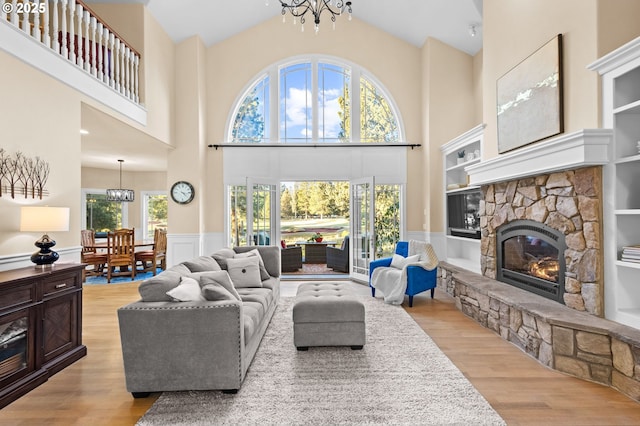 living room featuring light wood finished floors, a stone fireplace, and a notable chandelier