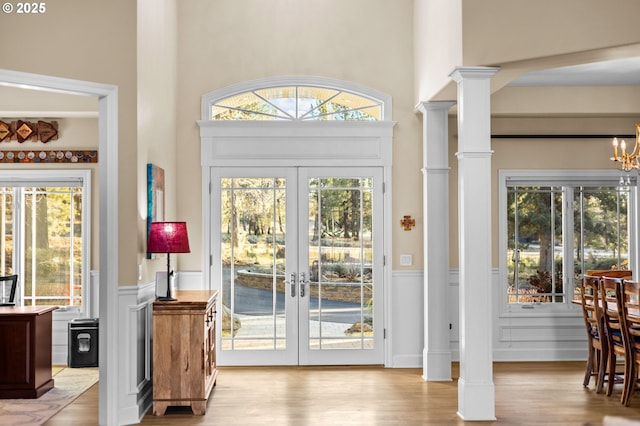 entryway with decorative columns, wainscoting, french doors, light wood-style floors, and a wealth of natural light