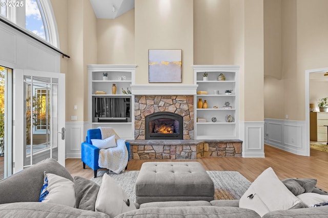 living room featuring built in features, a fireplace, a high ceiling, wainscoting, and light wood-type flooring