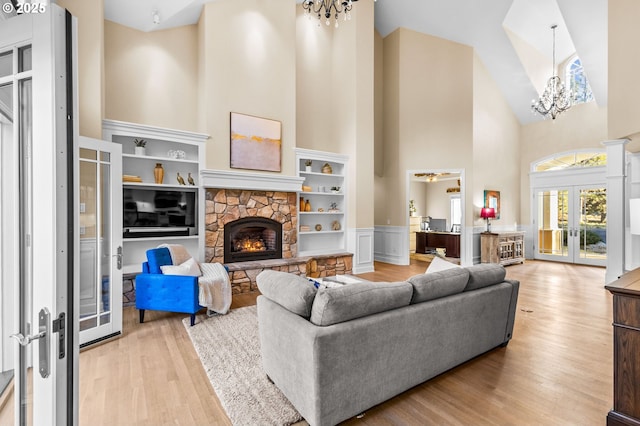 living area featuring light wood finished floors, french doors, a fireplace, high vaulted ceiling, and a notable chandelier