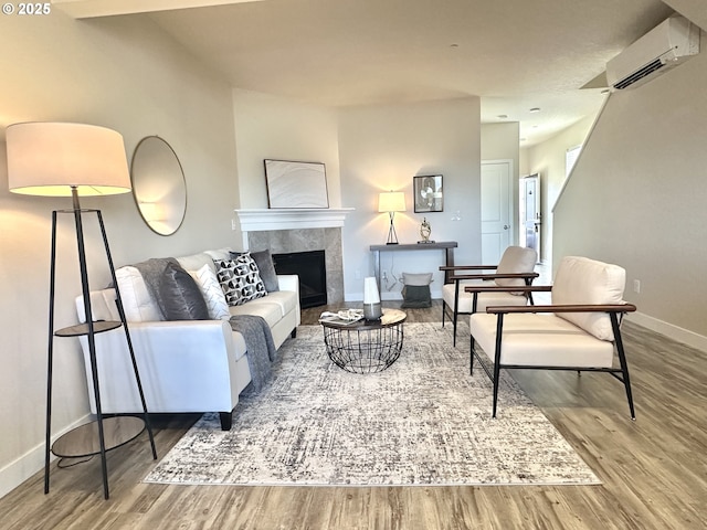 living room featuring an AC wall unit, baseboards, a tiled fireplace, and wood finished floors