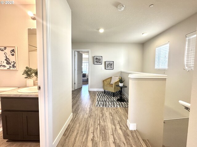 hall with plenty of natural light, a textured ceiling, an upstairs landing, and wood finished floors