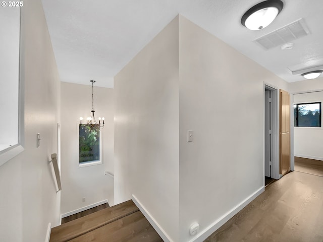 corridor featuring a chandelier, wood finished floors, visible vents, an upstairs landing, and baseboards