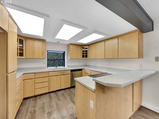 kitchen with a sink, light brown cabinets, a peninsula, and stainless steel dishwasher