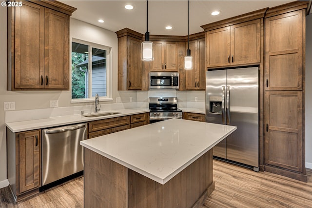 kitchen with stainless steel appliances, a sink, light wood finished floors, recessed lighting, and pendant lighting