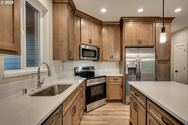 kitchen featuring appliances with stainless steel finishes, a sink, light wood-style flooring, recessed lighting, and decorative light fixtures