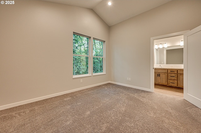 unfurnished bedroom with light colored carpet, vaulted ceiling, baseboards, and ensuite bathroom