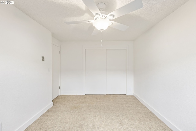 unfurnished bedroom with ceiling fan, a closet, light carpet, and a textured ceiling