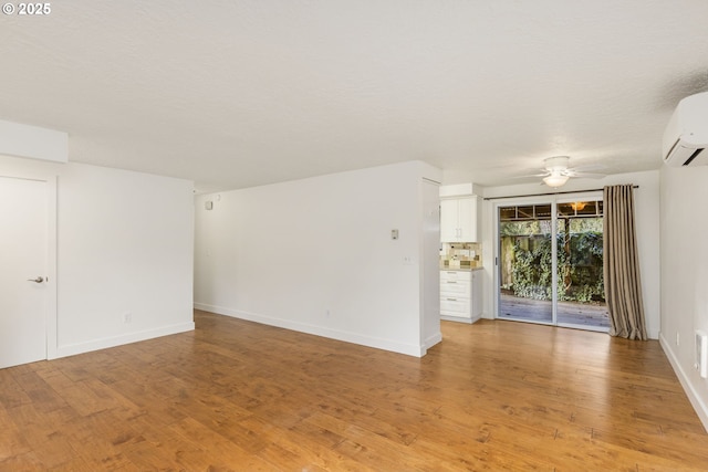 spare room featuring a wall mounted AC, ceiling fan, and light hardwood / wood-style floors