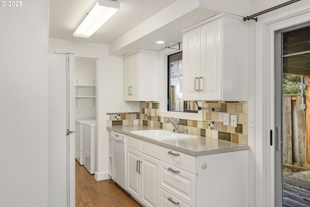 kitchen with sink, white cabinets, white dishwasher, decorative backsplash, and washer and dryer