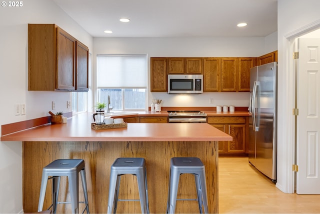 kitchen with light hardwood / wood-style floors, appliances with stainless steel finishes, a kitchen bar, and kitchen peninsula