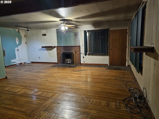 unfurnished living room featuring ceiling fan, baseboards, a brick fireplace, hardwood / wood-style flooring, and a textured ceiling