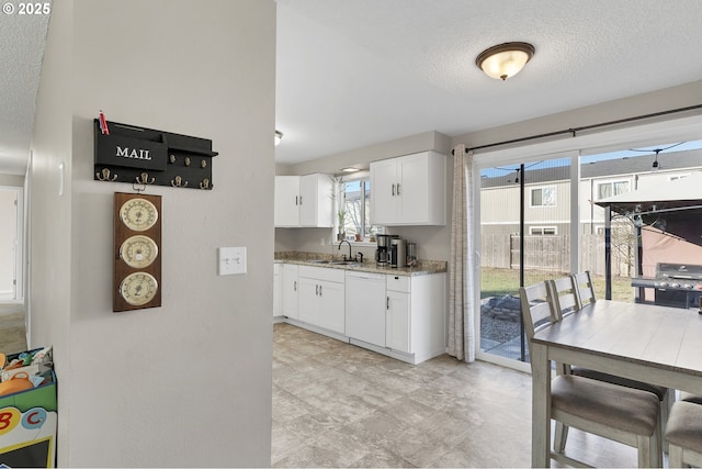 kitchen featuring white cabinetry, sink, white dishwasher, light stone countertops, and a textured ceiling