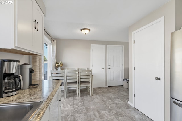 kitchen with stainless steel refrigerator, light stone countertops, and white cabinets