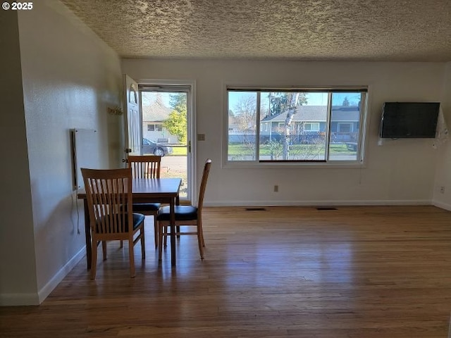 dining area featuring wood-type flooring, plenty of natural light, and a textured ceiling