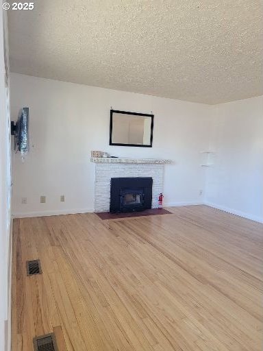 unfurnished living room featuring a brick fireplace, a textured ceiling, and light wood-type flooring