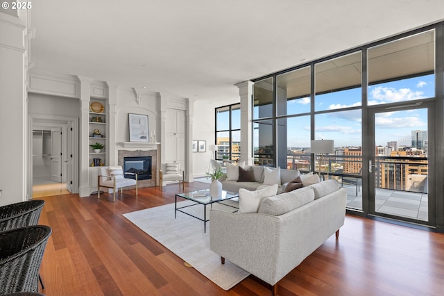 living room featuring a glass covered fireplace, built in shelves, expansive windows, wood finished floors, and a city view