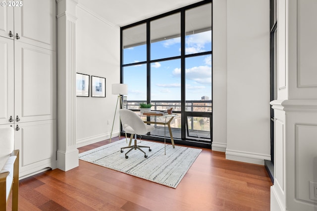 office space featuring baseboards, ornate columns, expansive windows, and wood finished floors