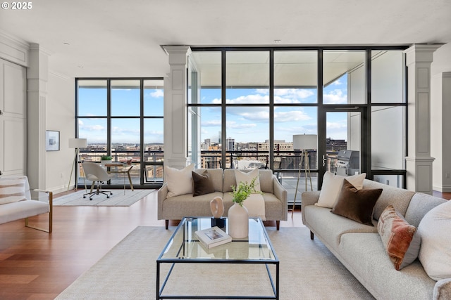 living room with decorative columns, wood finished floors, baseboards, expansive windows, and a city view
