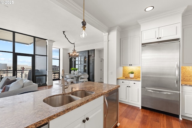 kitchen with decorative backsplash, built in fridge, a sink, a notable chandelier, and dark wood-type flooring