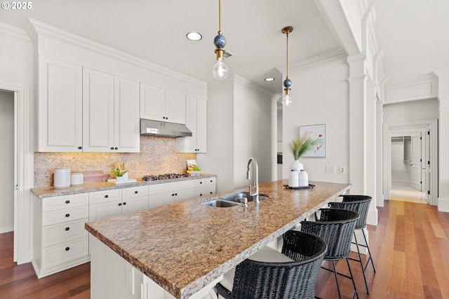 kitchen with wood finished floors, a sink, white cabinets, under cabinet range hood, and recessed lighting