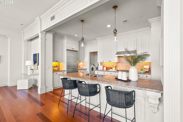 kitchen featuring decorative backsplash, a sink, built in refrigerator, under cabinet range hood, and recessed lighting